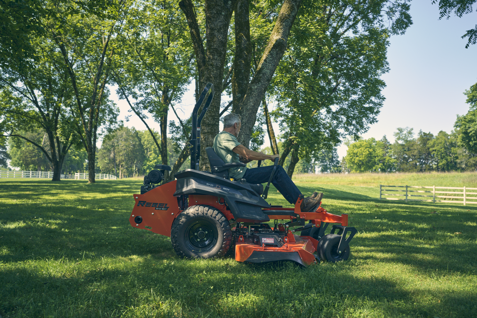 Person operating a riding lawn mower in a park-like setting with trees and grass.