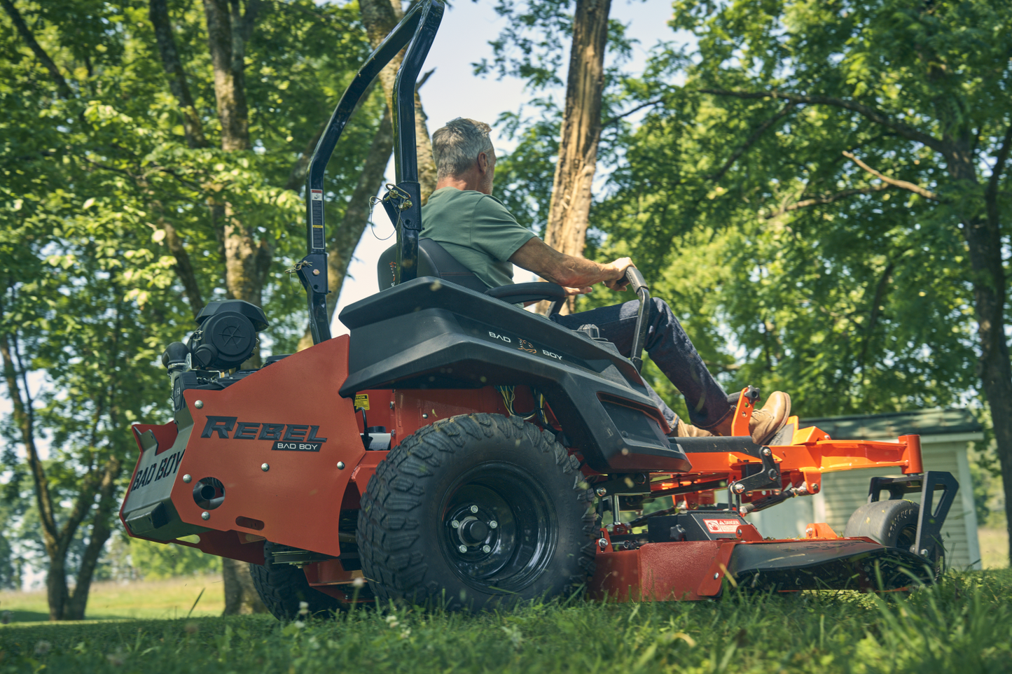 Person operating a red lawn mower in a grassy area with trees in the background