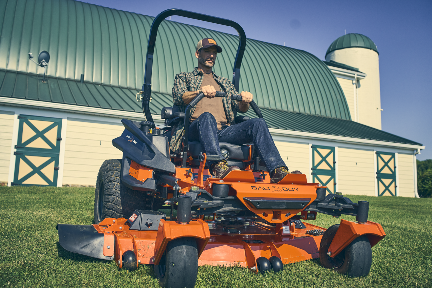 Man operating a large orange lawn mower in front of a barn.