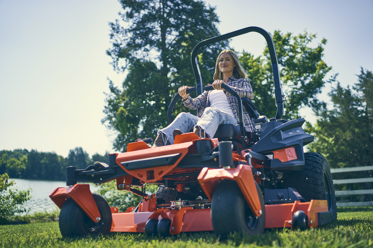 Person operating a large orange lawn mower in a grassy area with trees in the background