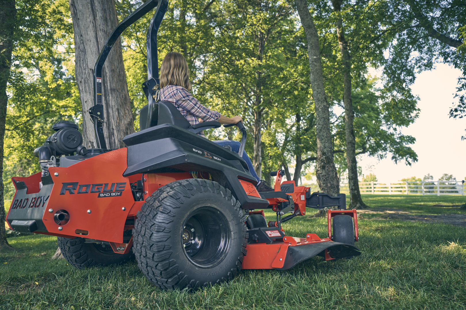 Person operating a red riding lawn mower in a park setting