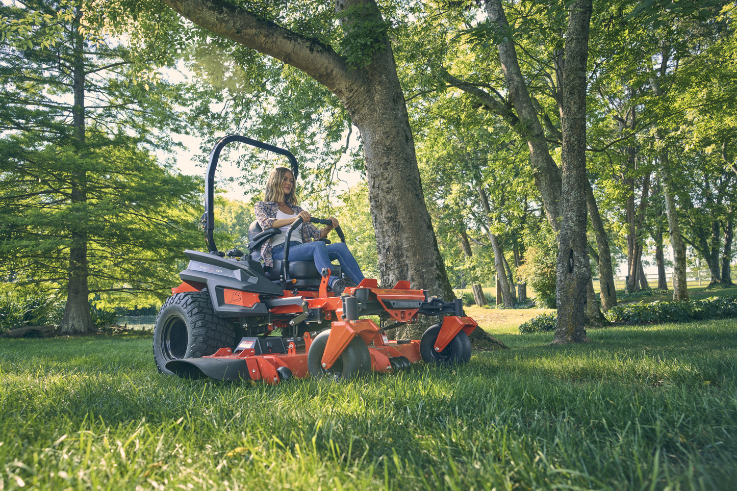 Person operating a red riding lawn mower in a park setting