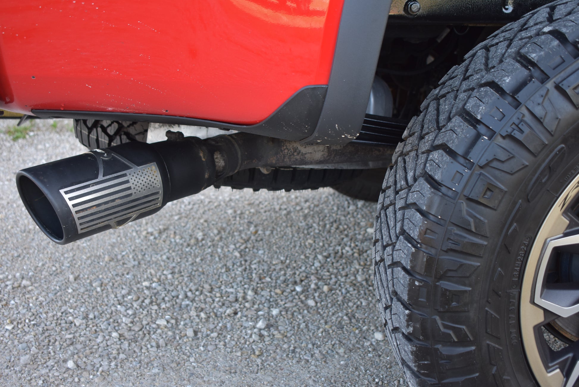 Close-up of a red vehicle's exhaust system and tire on a gravel surface.