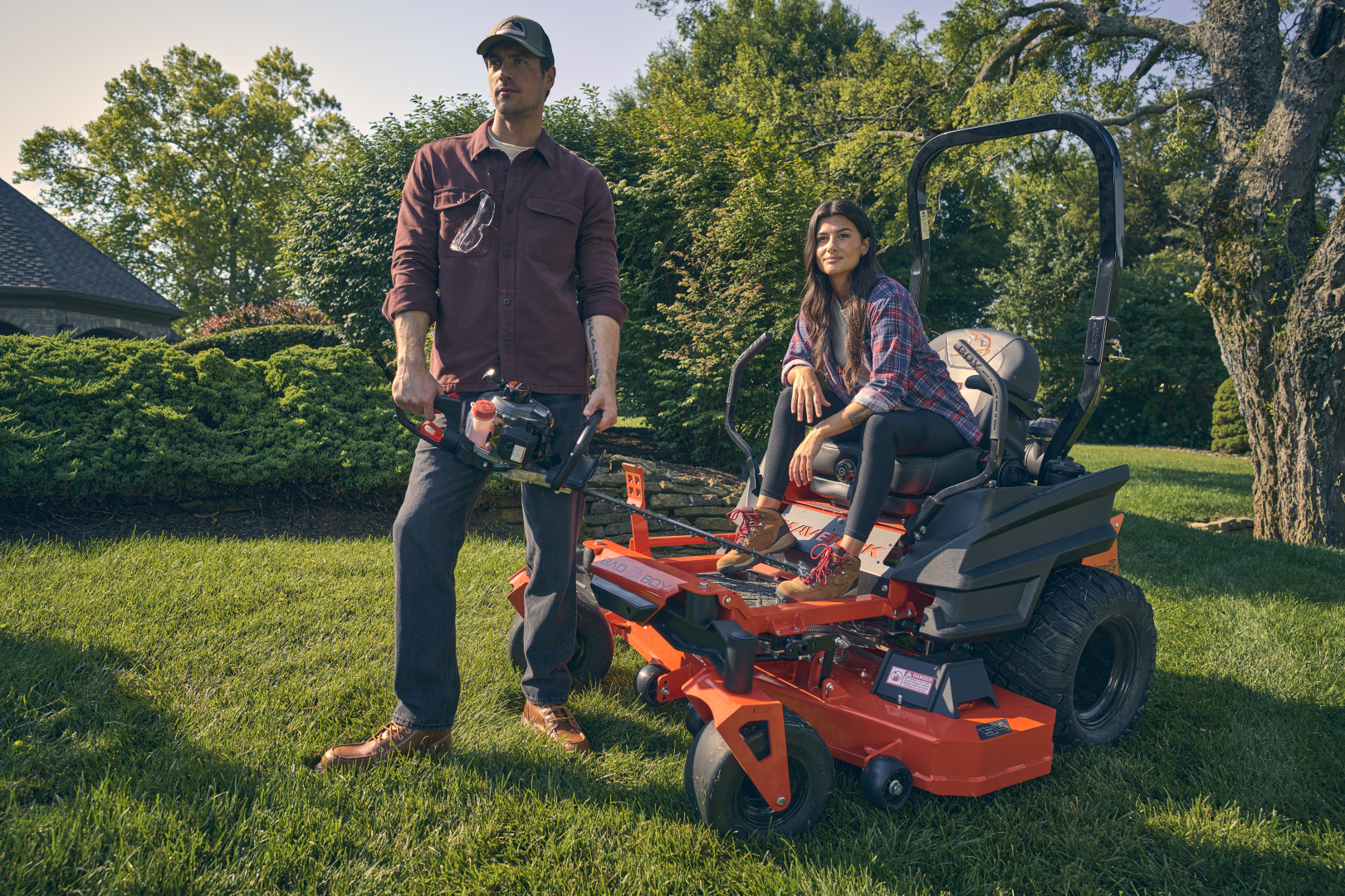 Man and woman with a riding lawn mower in a garden setting