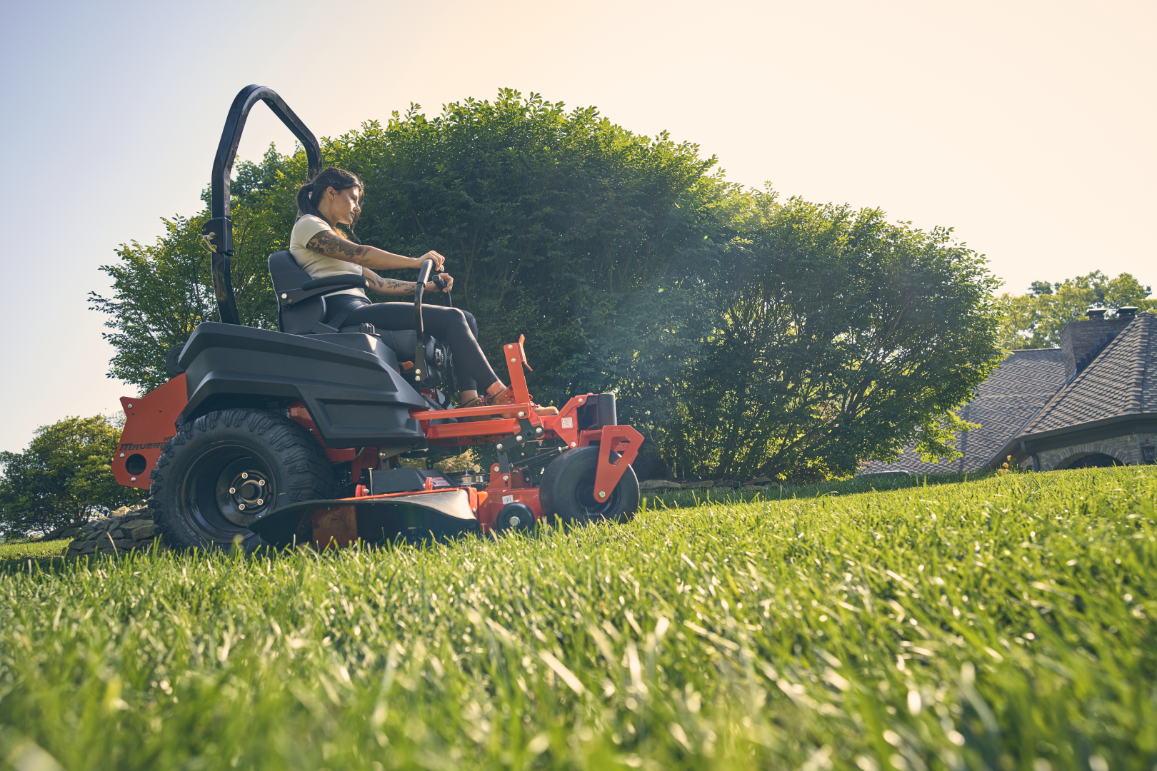 Person operating a lawn mower on a grassy area with trees in the background