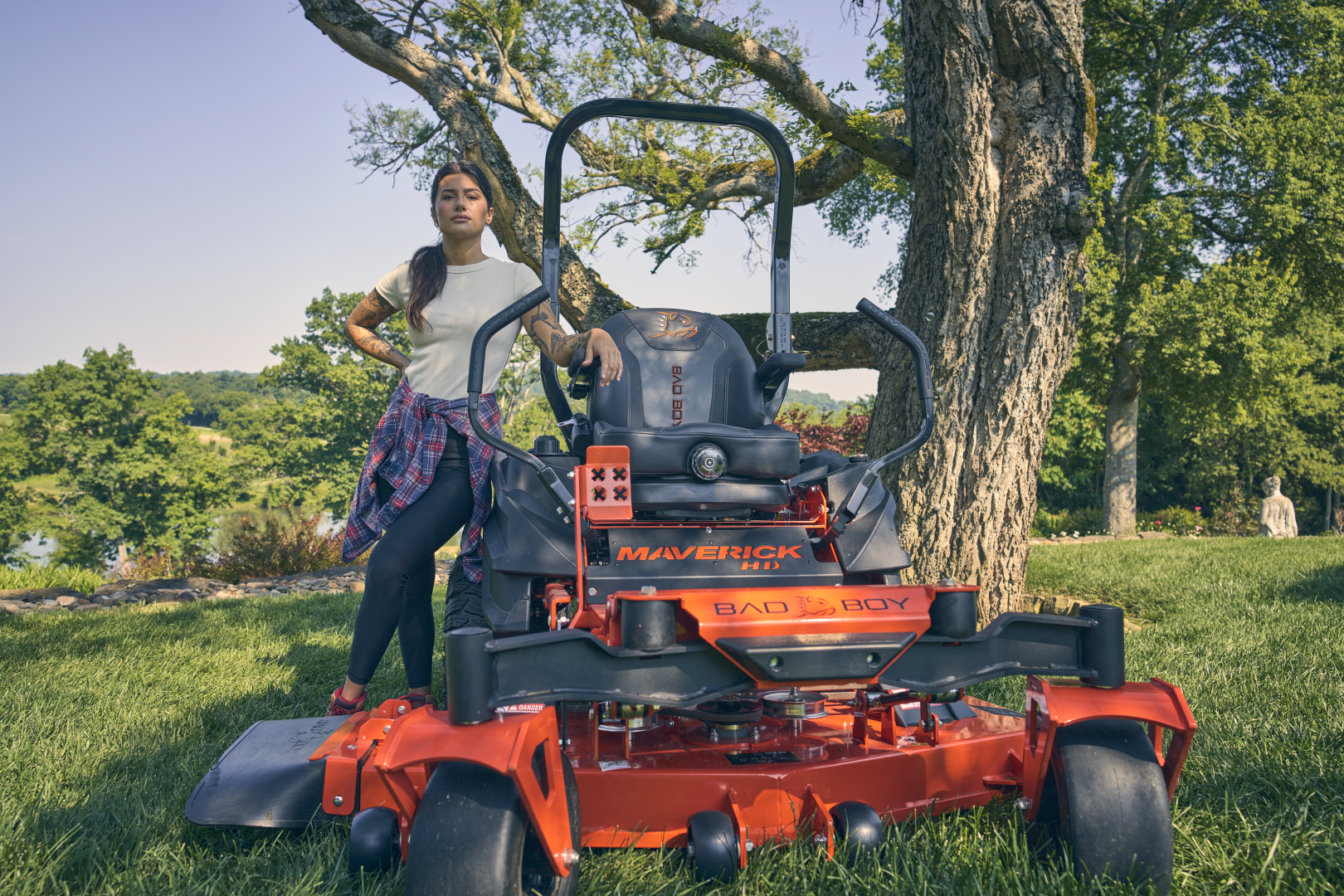 Person standing next to a red lawn mower under a tree