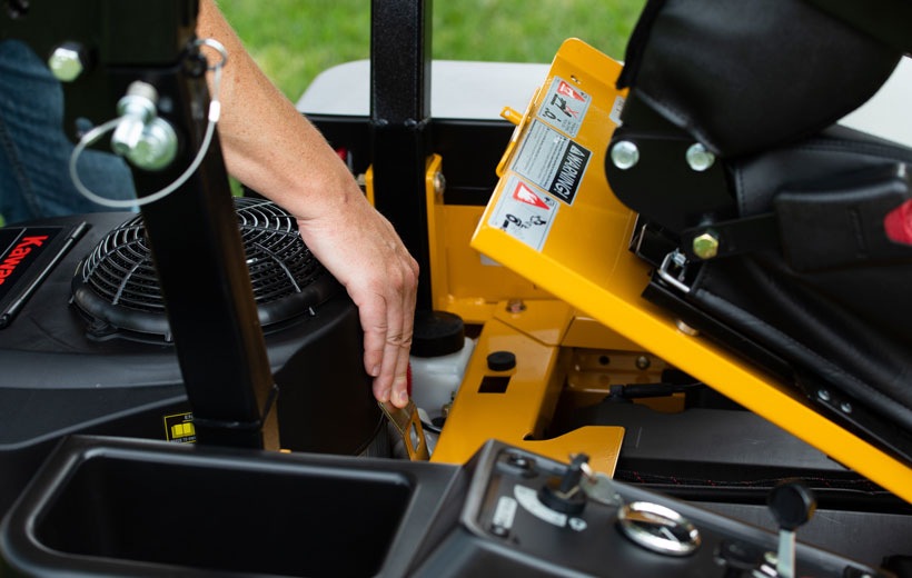 Person refueling a yellow lawn mower with grass visible in the background