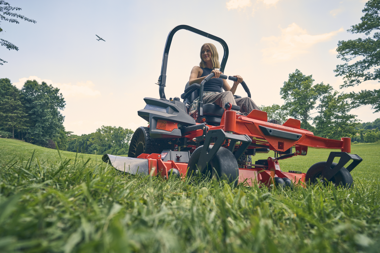 Person operating a red lawn mower on a grassy field with trees in the background