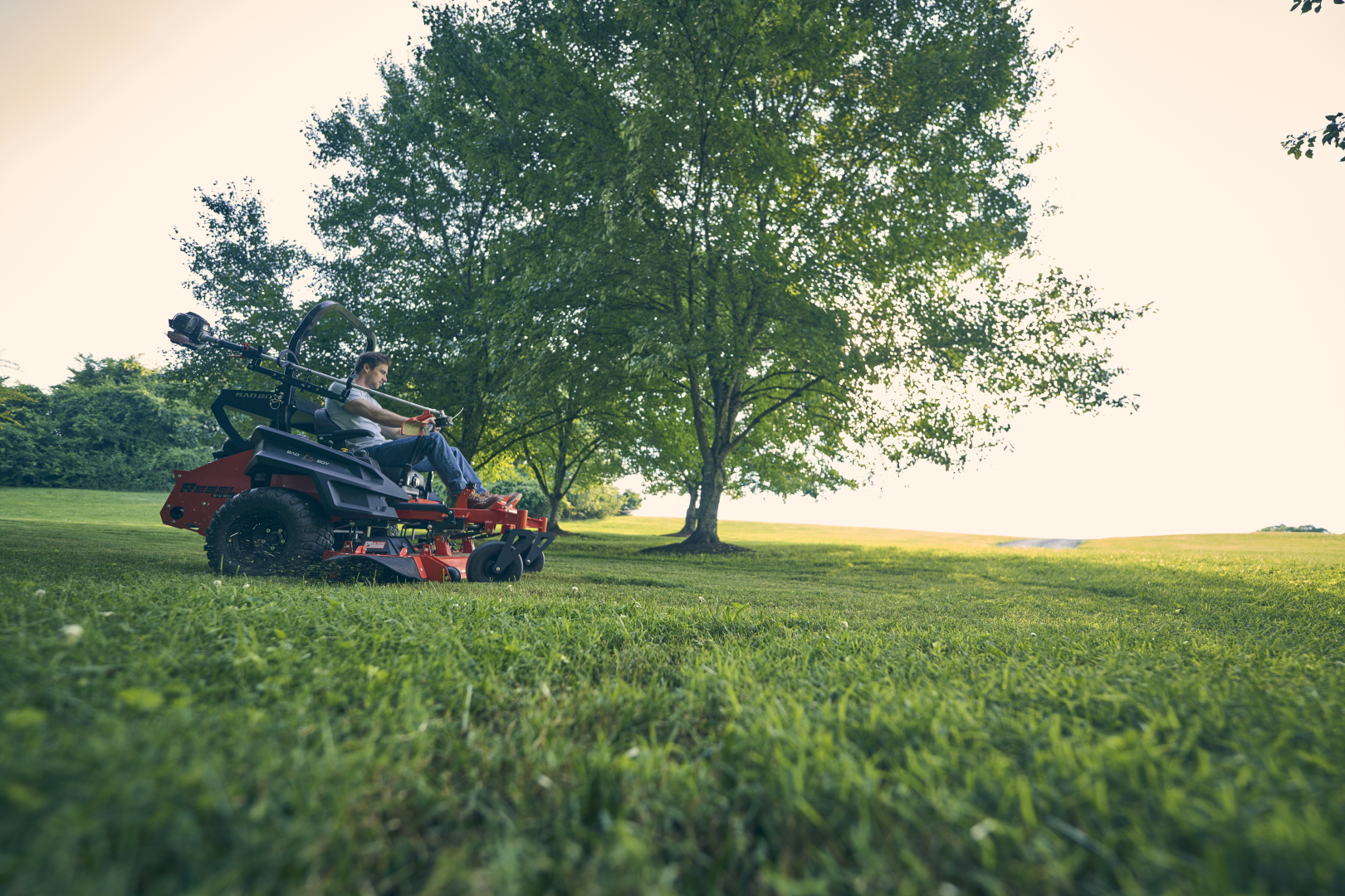 Person operating a riding lawn mower in a grassy area with trees in the background