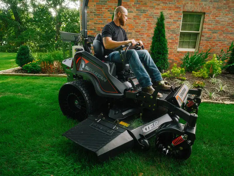 Man operating a riding lawn mower on a grassy area with a brick building in the background.