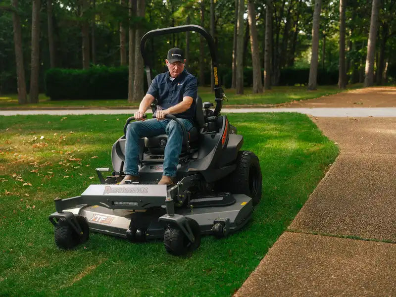 Person operating a large lawn mower on a grassy area with trees in the background
