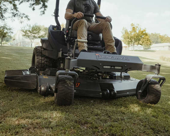 Person operating a riding lawn mower on a grassy area with trees in the background