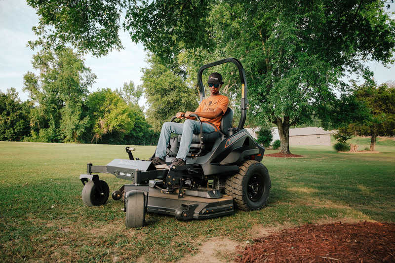 Person operating a large lawn mower in a grassy area with trees in the background
