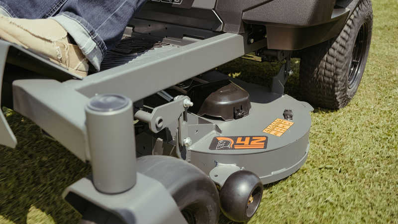 Close-up of a lawn mower on grass with a person partially visible.