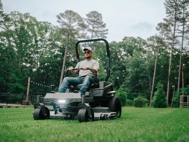 Man operating a riding lawn mower in a grassy area with trees in the background
