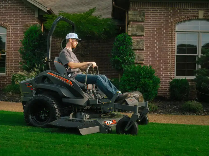 Man operating a riding lawn mower in front of a brick house