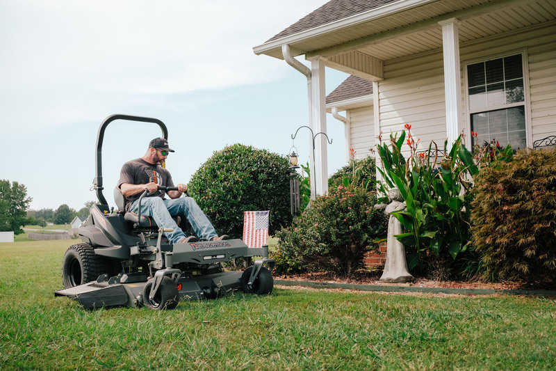 Man operating a riding lawn mower in front of a house
