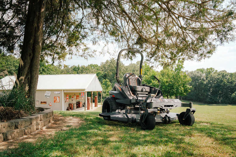 Large lawn mower on a grassy area with trees and a building in the background