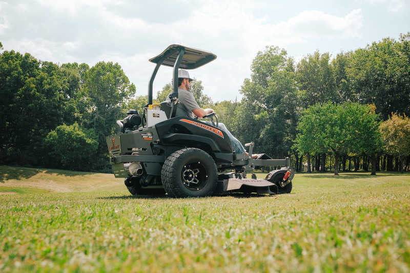 Person operating a large lawn mower in a grassy field with trees in the background