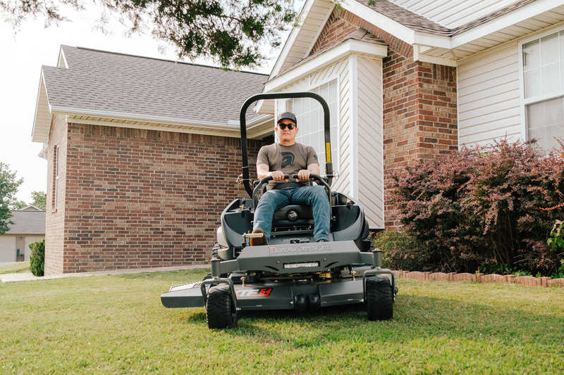 Man operating a riding lawn mower in front of a house