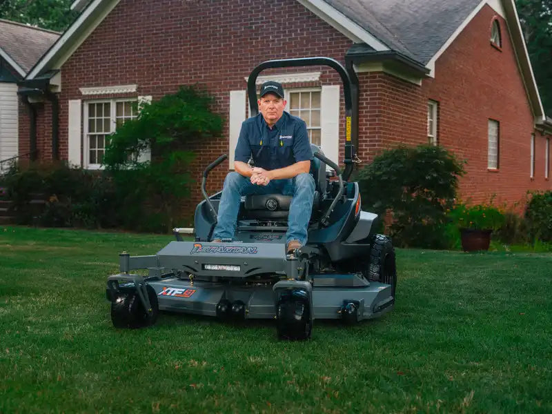 Man sitting on a riding lawn mower in front of a brick house