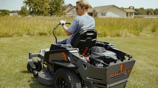 Person operating a Hustler lawn mower in a grassy field with houses in the background