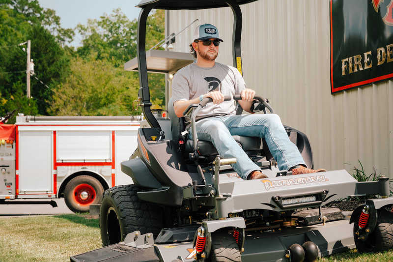 Man sitting on a large piece of equipment with a building and trees in the background
