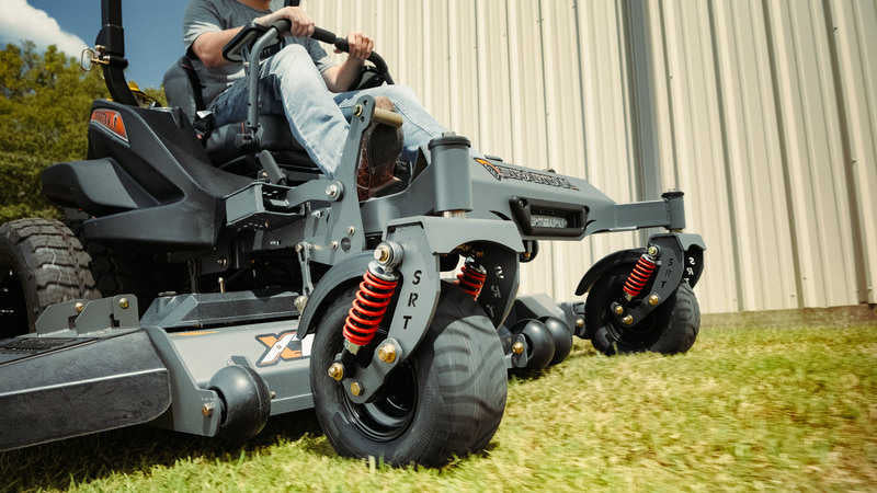 Person operating a riding lawn mower on grass with a building in the background
