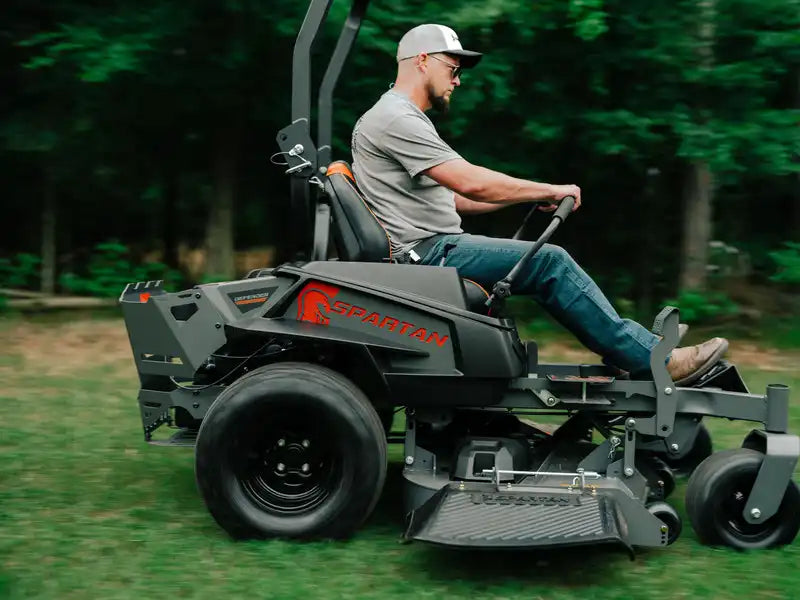 Man operating a Spartan riding lawn mower in a grassy area with trees in the background
