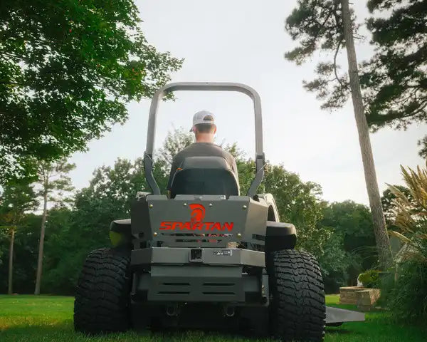 Person operating a Bobcat lawn mower in a park-like setting with trees and grass.