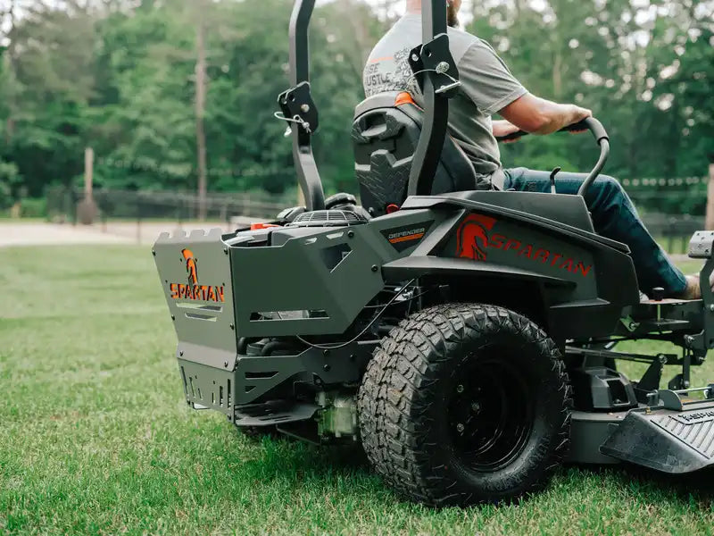Person operating a lawn mower on a grassy field with trees in the background