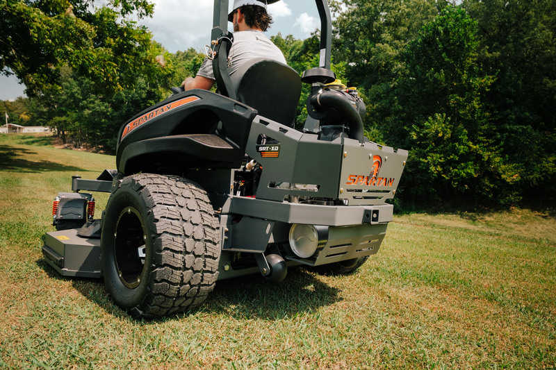 Person operating a riding lawn mower in a grassy area with trees in the background