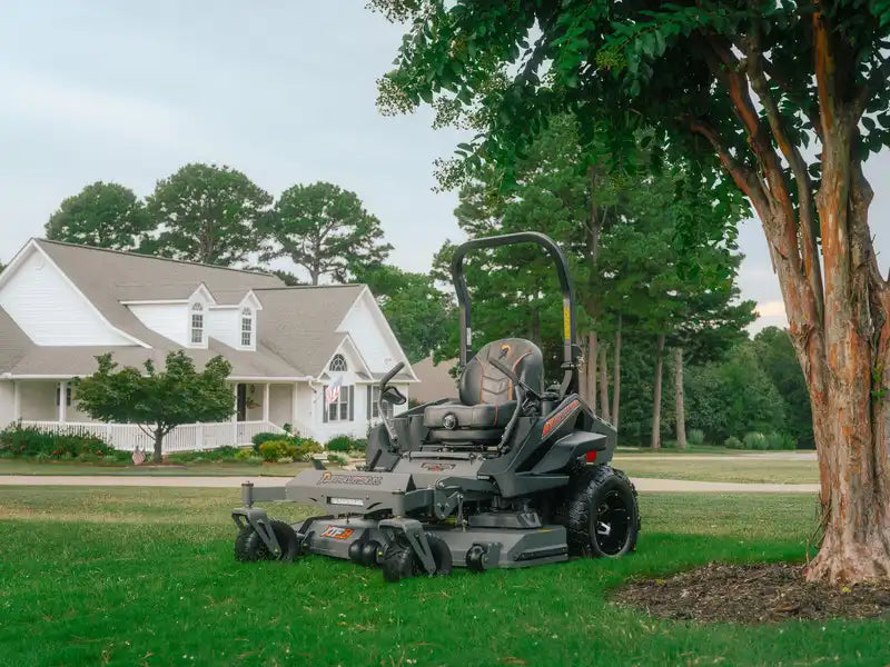 Large lawn mower on a grassy area with a house and trees in the background
