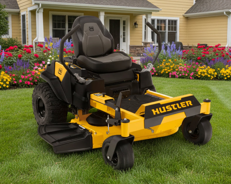 Yellow and black Hustler riding lawn mower in a garden setting with flowers and a house.