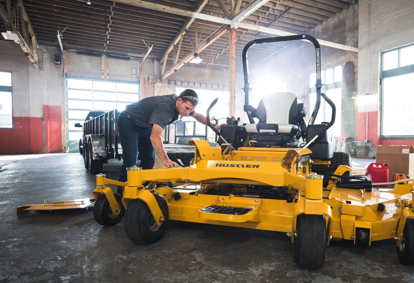 Person working on a yellow Hustler zero-turn lawn mower in a warehouse.