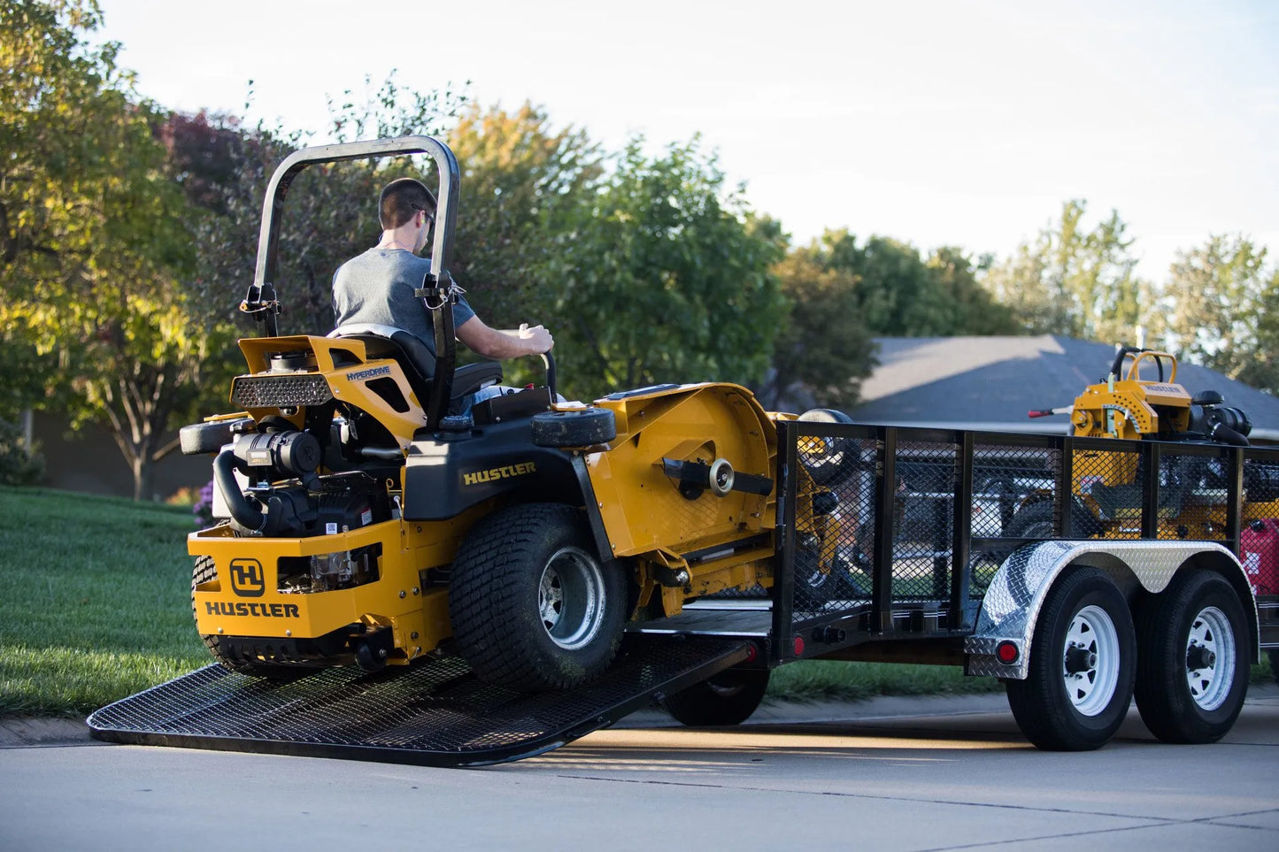 Yellow Hustler mower being loaded onto a trailer with a person inside.