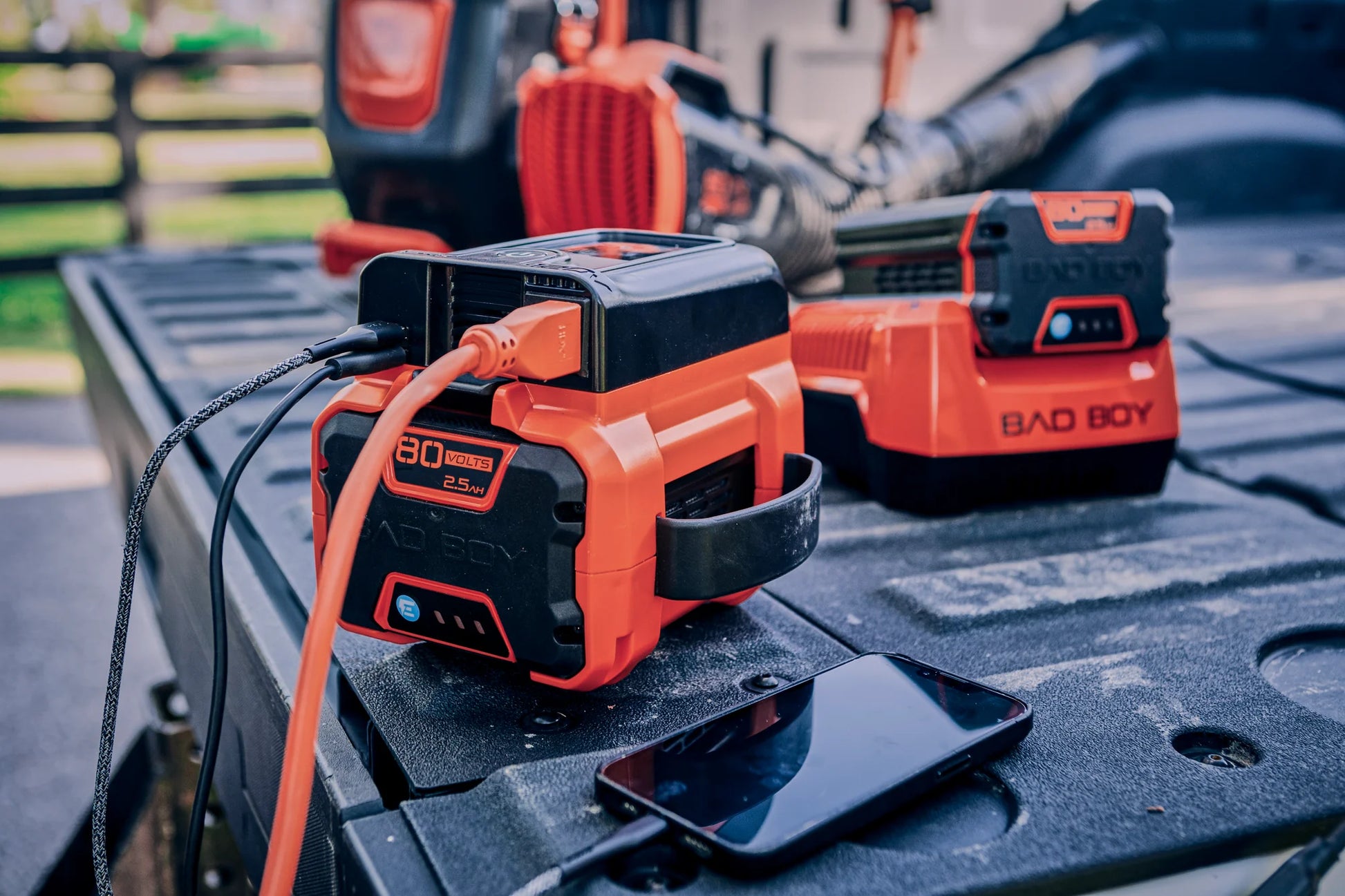 Two Bad Boy power tools on a truck bed with a smartphone nearby.