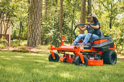 Person operating a red riding lawn mower in a grassy area with trees.