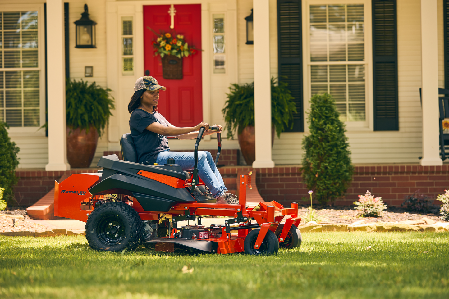 Person using a riding lawn mower in front of a house with a red door.