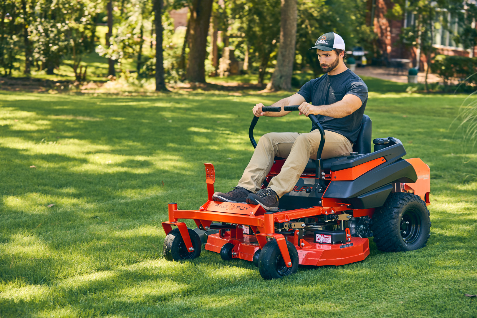 Man operating a red riding lawn mower on a green lawn with trees in the background