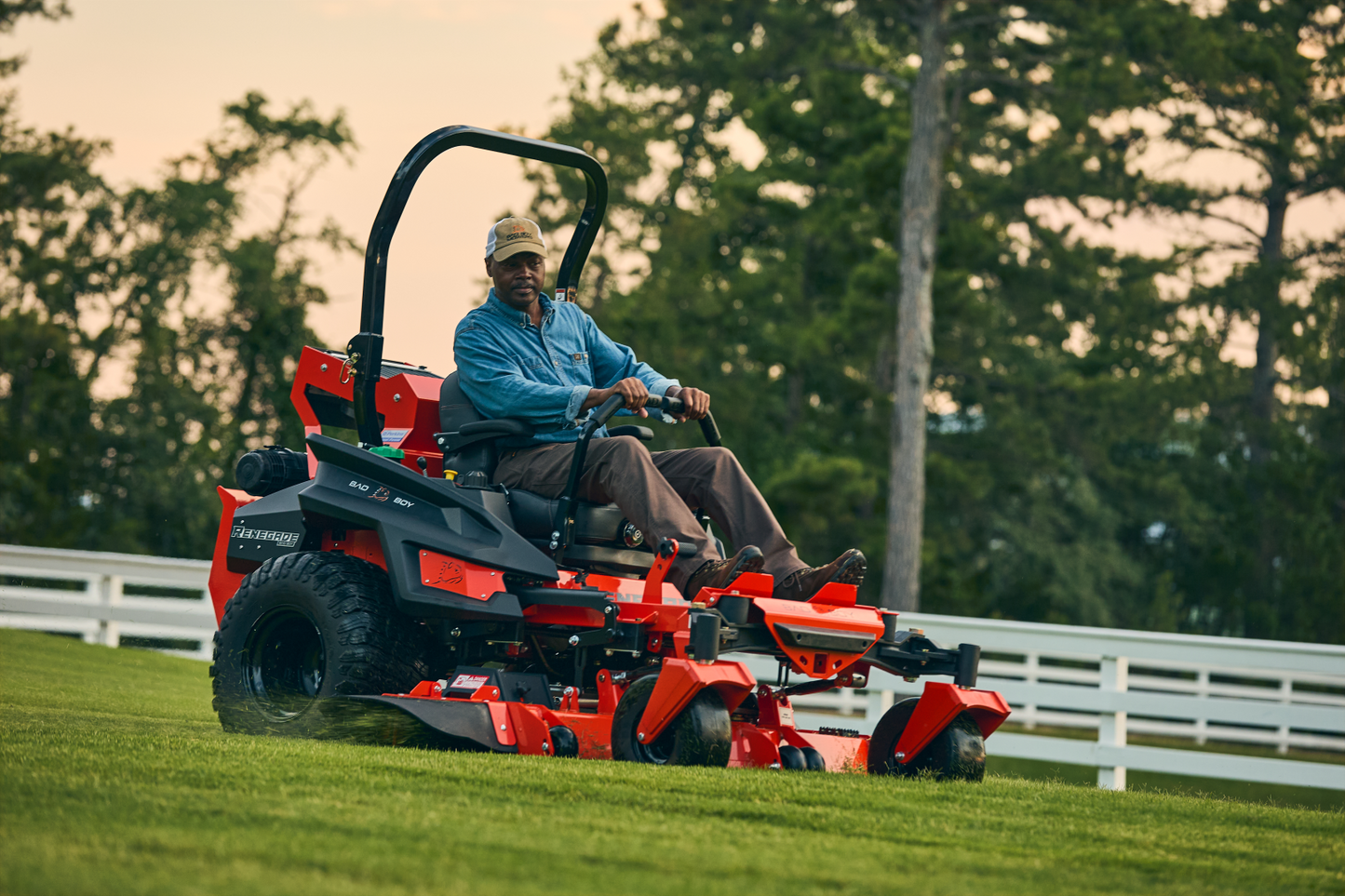 Man operating a red riding lawn mower in a grassy field with trees in the background.