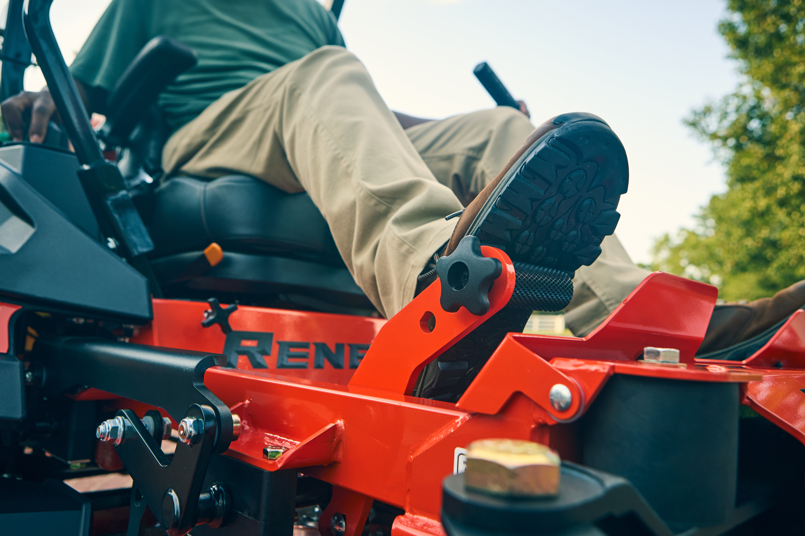 Person operating a red riding lawn mower with 'Reno' branding.