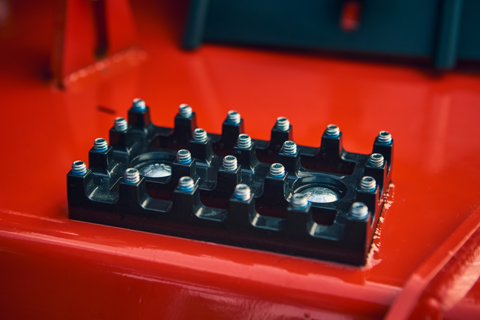 Close-up of a black metal bracket with screws on a red background