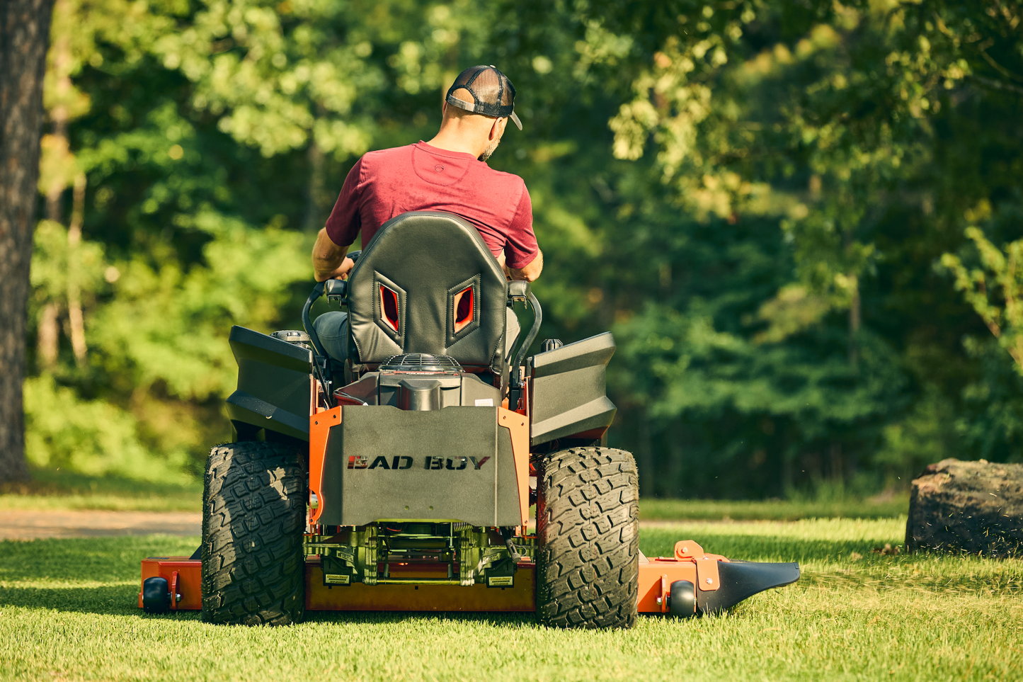 Person operating a lawn mower on a grassy area with trees in the background