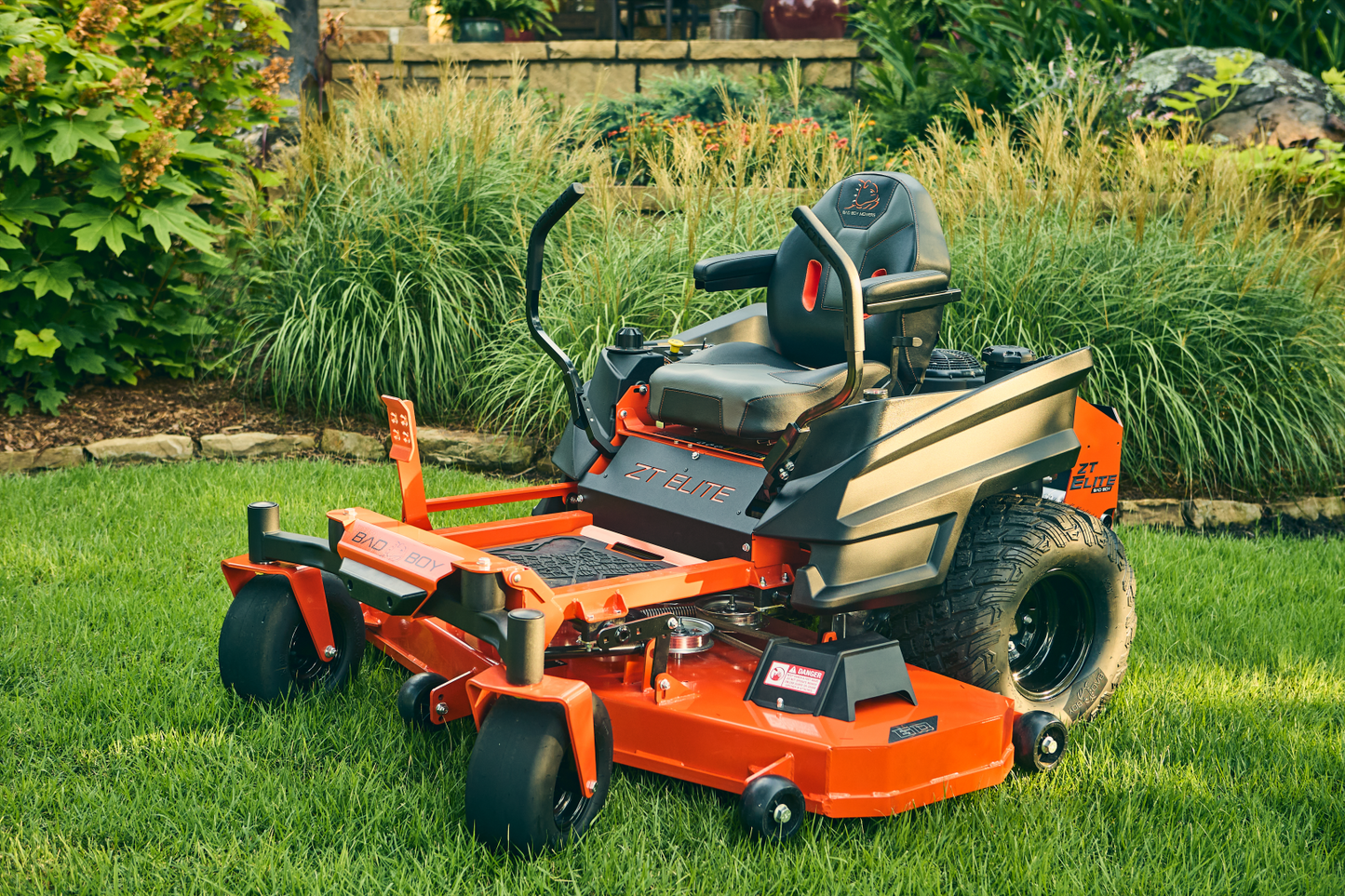Orange riding lawn mower on a grassy area with garden plants in the background