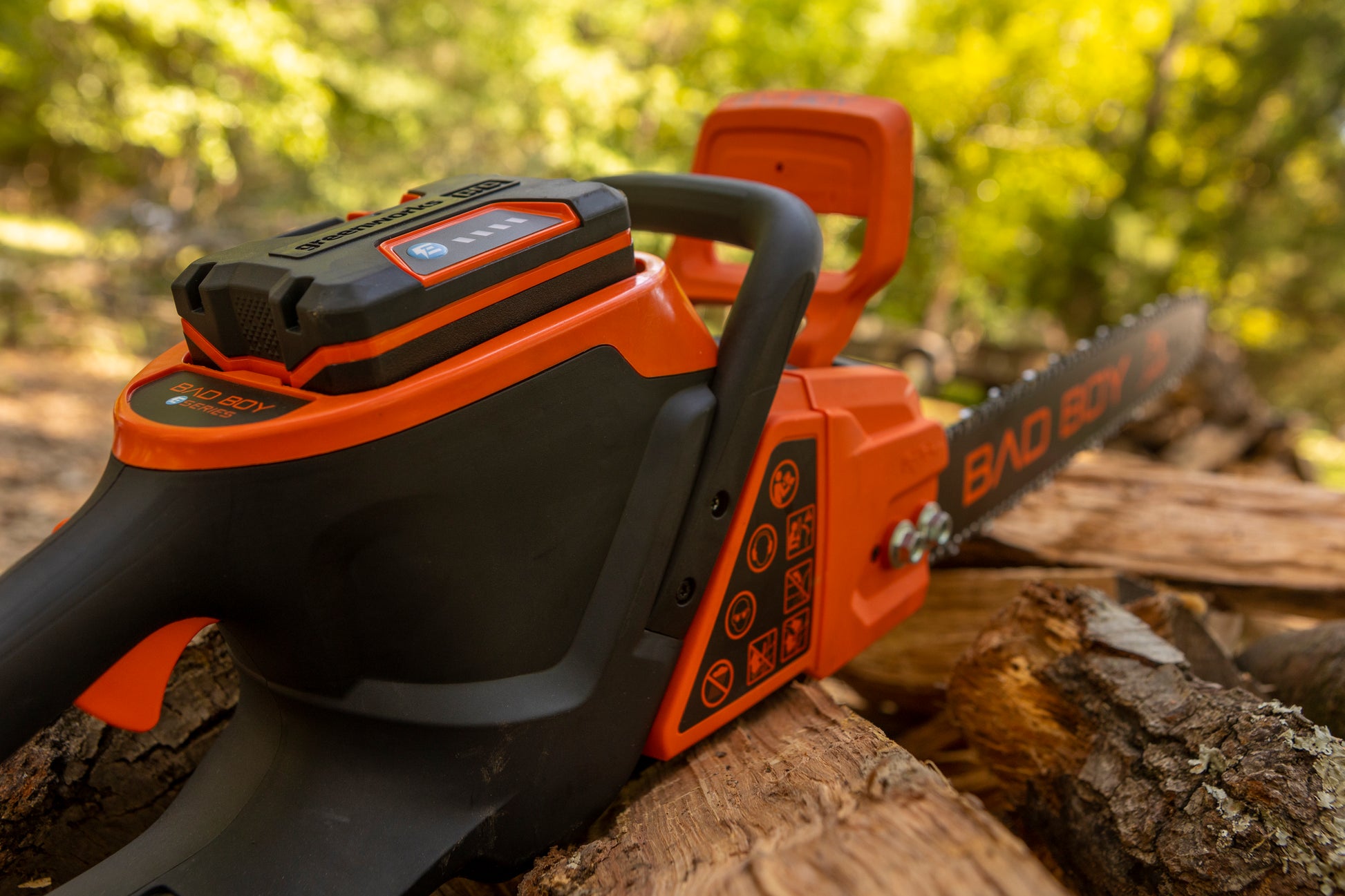 Orange and black chainsaw on a log with blurred greenery in the background