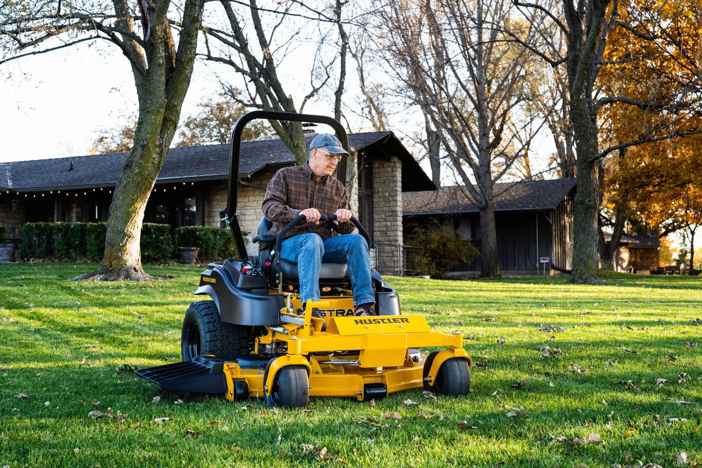 Person operating a yellow riding lawn mower on a grassy area with trees and a house in the background.