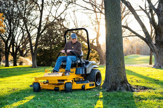 Man operating a yellow riding lawn mower in a park setting with trees and grass.