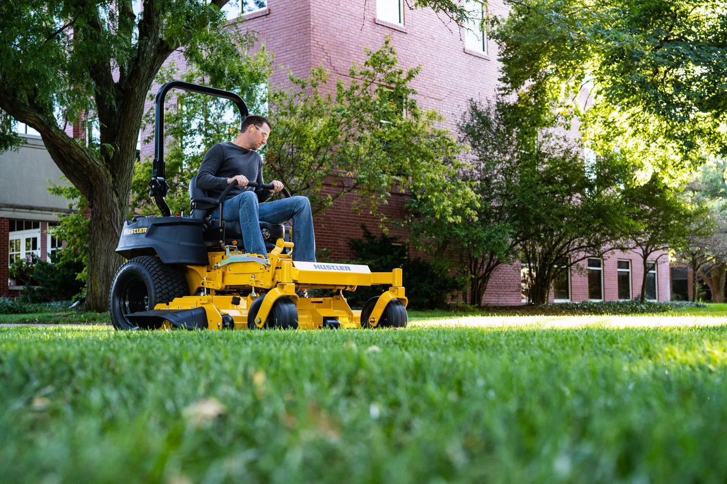 Man operating a yellow lawn mower in a residential area with trees and houses in the background.