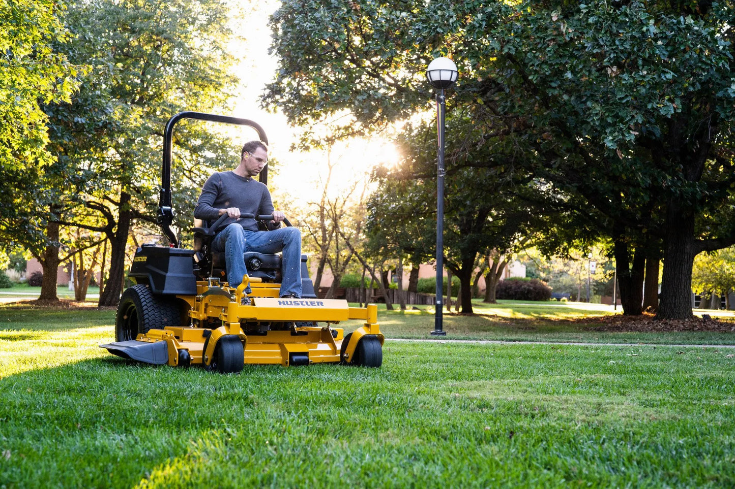 Person operating a yellow riding lawn mower in a park setting with trees and grass.